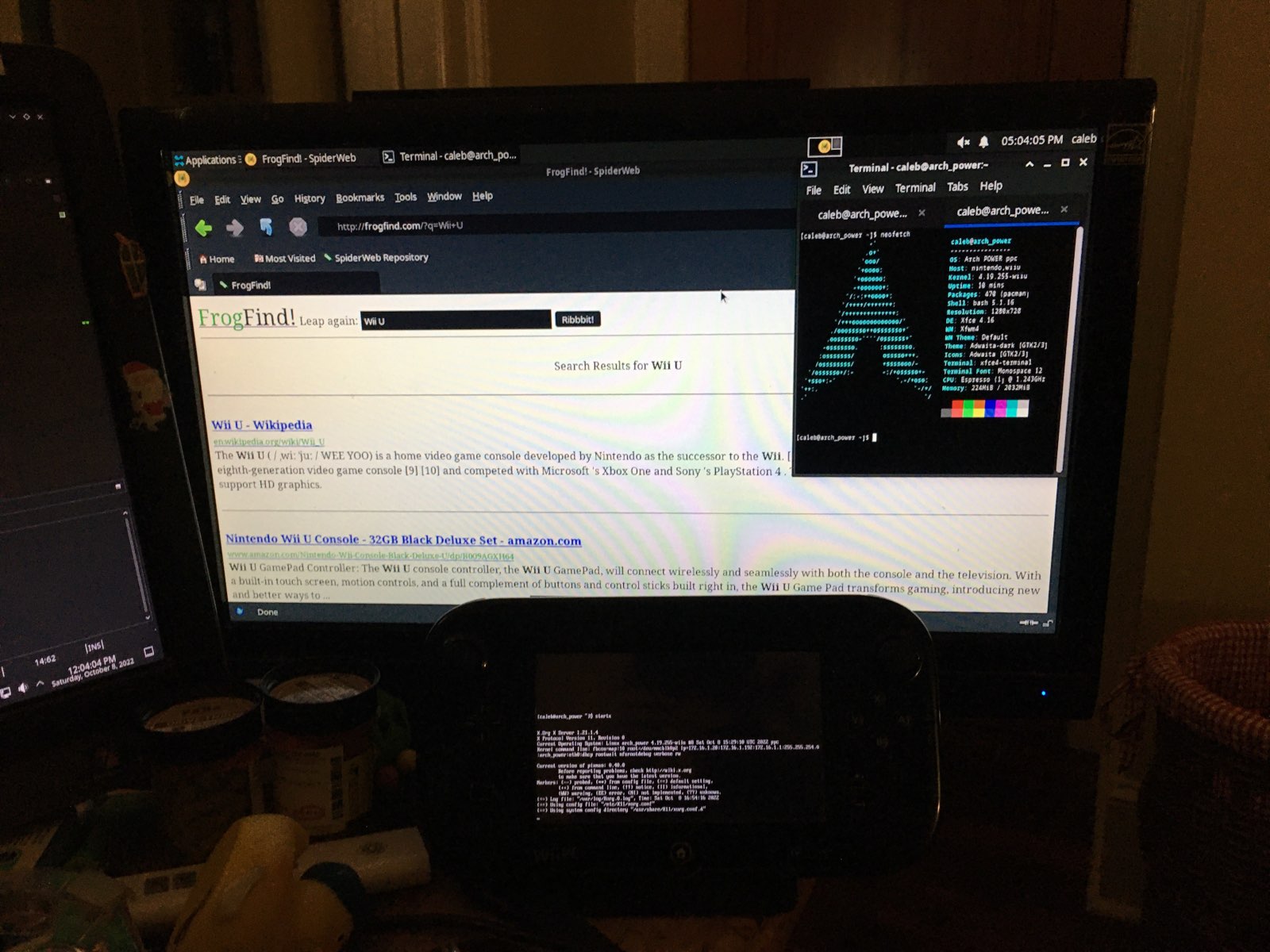 A monitor showing a web browser and FrogFind, with an Arch neofetch in the corner. A Wii U GamePad sits below it with some Xorg log output.